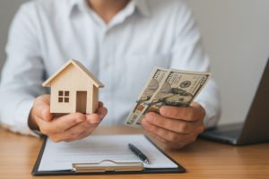 Osoba siedząca przy drewnianym stole i przeglądająca dokumenty finansowe związane z kredytem hipotecznym; na stole znajduje się kalkulator, notes i laptop w jasnym, domowym wnętrzu